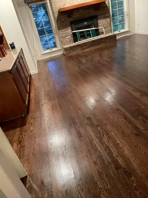 Living room with dark hardwood floors, stone fireplace, and large windows