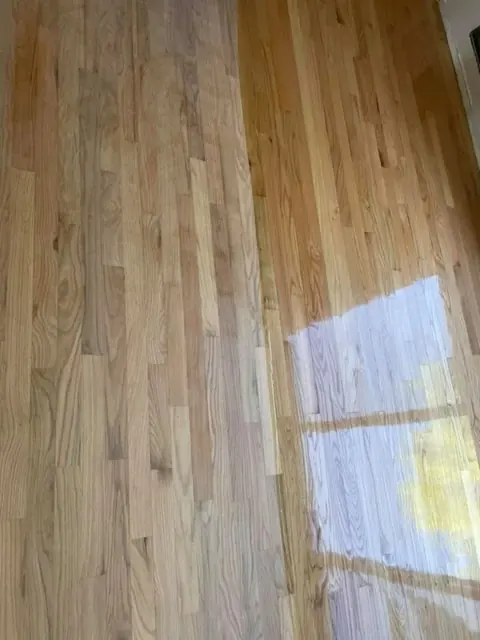 Wood floor halfway through refinishing — dull unfinished left side contrasts with glossy right side