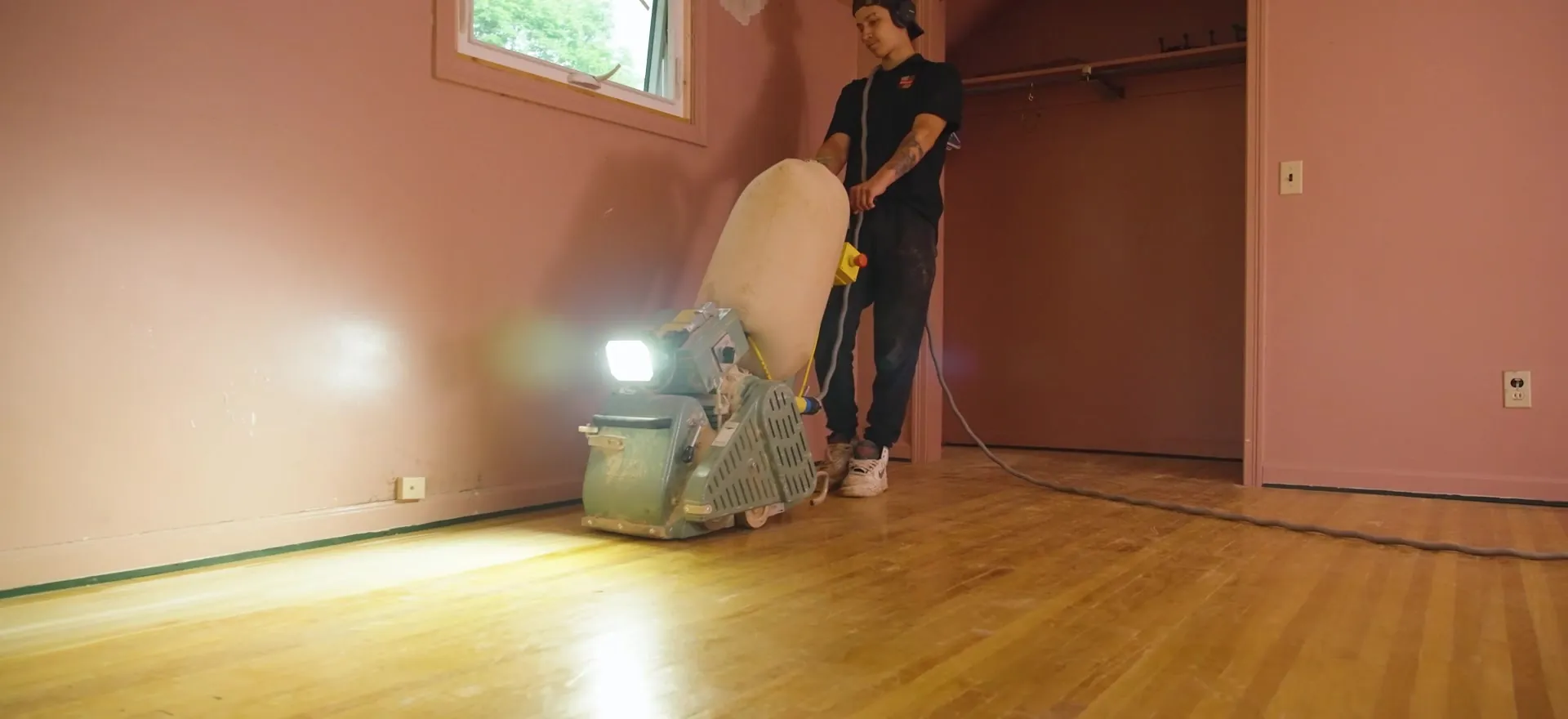 A Monroe Floor Resurfacing crew member sanding a hardwood floor with a drum sander